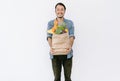 Healthy positive young Asian man holding paper shopping bag full of fresh vegetables and groceries with copy space isolated on Royalty Free Stock Photo