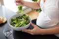 Pregnant woman eating a green salad at home