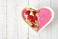 Raspberry smoothie in a heart bowl with superfoods over white wood.