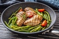 Healthy recipe of grilled chicken, green vegetable and tomatoes on a dark nonstick pan placed on metalic grid and dark