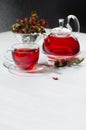 Healthy red herbal tea in transparent teapot, cup with hawthorn berries, rose hip, dry leaves in sunlight in contrast black. Royalty Free Stock Photo