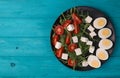 healthy salad of arugula spinach tomatoes feta cheese and boiled eggs in a black round kitchen plate, top view. useful on a diet