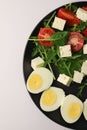 healthy salad of arugula spinach tomatoes feta cheese and boiled eggs in a black round kitchen plate, top view. useful on a diet