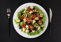 Healthy salad of cherry tomatoes, cucumbers, peppers, black olives, quail eggs and gorgonzolla cheese on black