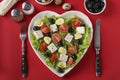 Healthy salad with cherry tomatoes, feta, quail eggs, black olives and microgreens peas on a heart-shaped plate on a red Royalty Free Stock Photo