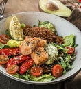 Healthy salad with fillet salmon, quinoa, avocado sauce, grilled pepper, tomatoes, lettuce, arugula in plate on wooden background Royalty Free Stock Photo