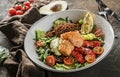 Healthy salad with fillet salmon, quinoa, avocado sauce, grilled pepper, tomatoes, lettuce, arugula in plate on wooden background Royalty Free Stock Photo