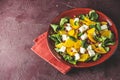 Healthy salad with persimmon, doucette lambs-lettuce, cornsalad, feld salad and feta cheese on a red plate on a red background. Royalty Free Stock Photo