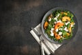 Healthy salad with persimmons, arugula, feta cheese and pumpkin seeds on a dark plate