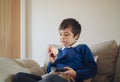 Healthy School kid eating red apple while watching TV, Portrait child eating fresh fruit for breakfast. Happy boy sitting on sofa