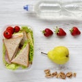 Healthy school lunch box with fresh fruits, walnuts, organic vegetables sandwiches and bottle of water on white wooden background, Royalty Free Stock Photo