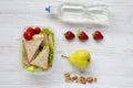 Healthy school lunch box with fresh fruits, walnuts, organic vegetables sandwiches and bottle of water on white wooden table, flat Royalty Free Stock Photo