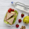 Healthy school lunch box with fresh organic vegetables sandwiches, walnuts, bottle of water and fruits on white wooden surface, o Royalty Free Stock Photo