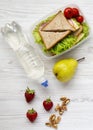 Healthy school lunch box with fresh organic vegetables sandwiches, walnuts, bottle of water and fruits on a white wooden table,
