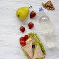 Healthy school lunch box with fresh organic vegetables sandwiches, walnuts, bottle of water and fruits on white wooden table, over Royalty Free Stock Photo