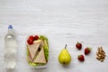 Healthy school lunch box with fresh organic vegetables sandwiches, walnuts, fruits and bottle of water on white wooden background, Royalty Free Stock Photo