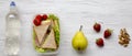 Healthy school lunch box with fresh organic vegetables sandwiches, walnuts, fruits and bottle of water on white wooden surface, ov Royalty Free Stock Photo