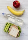 Healthy school lunch box with sandwich, fruits and bottle of water on white wooden surface, flat lay. From above, top view,