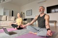 Senior couple meditating doing virtual yoga poses watching online class at home.