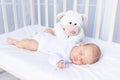 healthy sleep of a newborn baby in a crib in the bedroom with a soft toy bear on a cotton bed Royalty Free Stock Photo