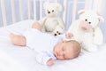 Healthy sleep of a newborn baby in a crib in the bedroom with a soft toy bear on a cotton bed Royalty Free Stock Photo