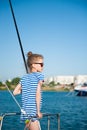Healthy small caucasian girl in sunglasses and striped sailor shirt standing on board of boat in sea port during summer Royalty Free Stock Photo
