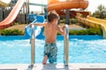 Healthy small kid enters blue swimming pool in water park with water tube slides in summer