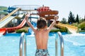 Healthy happy little kid near blue swimming pool in water park with water tube slides in summer