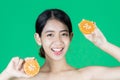 Healthy smiling young Asian woman holding two halves of oranges over green isolated background. Healthy and beauty skin care Royalty Free Stock Photo