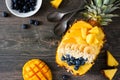 Smoothie bowl in a pineapple with coconut, bananas, mango & blueberries, top view on dark wood Royalty Free Stock Photo