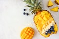 Smoothie bowl in a pineapple with coconut, bananas, mango & blueberries, top view on marble with copy space Royalty Free Stock Photo