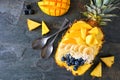 Smoothie bowl in a pineapple with coconut, bananas, mango & blueberries, top view on slate with copy space Royalty Free Stock Photo