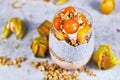 Smoothie with chia seeds in vegan coconut milk and joghurt, mixed with cereals and topped with orange persimmon and physalis