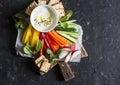 Healthy snack - raw vegetables and yogurt sauce on a wooden cutting board, on a dark background, top view. Vegetarian healthy food