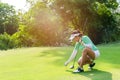 Healthy Sport.  Asian sporty woman putting golf ball on tee with club in golf course on evening on time for healthy sport. Royalty Free Stock Photo
