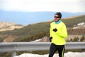 Healthy sport man running on asphalt road at snow mountains in trail runner hard workout in winter Royalty Free Stock Photo