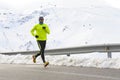 Healthy sport man running on asphalt road at snow mountains in trail runner hard workout in winter