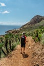 Healthy sporty woman traveler hiking in Sicily,sea and mountains in background.Solo girl with baseball cap enjoying climbing and Royalty Free Stock Photo