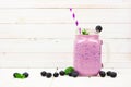 Healthy blueberry smoothie in a mason jar with scattered fruit against white wood