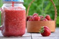 Healthy strawberry smoothie in a mason a jar mug over a rustic wood background against of green foliage in the garden Royalty Free Stock Photo