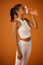 Healthy, studio or Indian woman drinking water for fitness, hydration or workout break on orange background. Tired girl Royalty Free Stock Photo