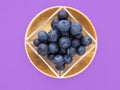 Healthy superfood blueberries in glass square bowl on beautiful gold coloured plate, on purple. Pretty food still life.