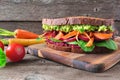 Healthy superfood sandwich with avocado, beet hummus, spinach radishes and carrots, table scene against dark wood