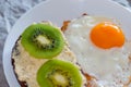 Healthy and tasty breakfast, wholemeal bread sandwich with kiwi and a fried egg on a white plate, close-up, top view