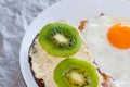 Healthy and tasty breakfast, wholemeal bread sandwich with kiwi and a fried egg on a white plate, close-up, top view