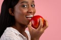 Healthy teeth concept. Pretty black woman with beautiful smile biting fresh red apple on pink studio background Royalty Free Stock Photo