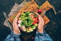 Healthy vegan salad, avocado, celery, cucumber, tomato, radish, nuts and seeds. Girl in denim blouse holding a bowl of vegan salad