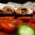 Healthy vegetarian breakfast concept: rolled cheese tacos on red plate with sliced tomatoes and cucumbers on cutting board Royalty Free Stock Photo