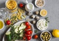 Healthy vegetarian food ingredients - pasta, zucchini, tomatoes, herbs, spices, vegan cheese, olive oil, lemon, olives. On a gray