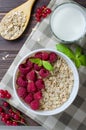 Healthy vegetarian food. Oatmeal with raspberry. Wooden spoon with cereals, milk in a glass, red currant. Brown wooden background Royalty Free Stock Photo